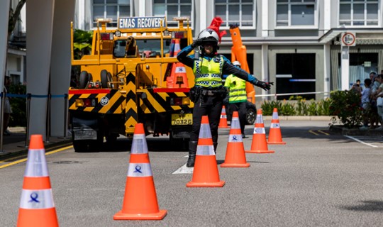 Image of of LTA's Traffic Marshal blowing a whistle and directing traffic, while on a road with LTA orange cones